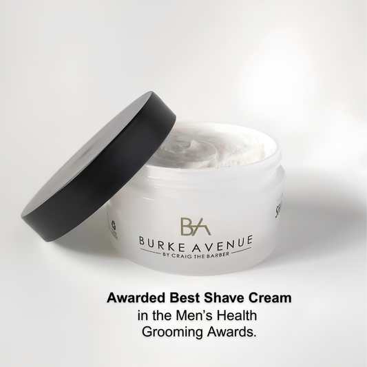 A white jar of Burke Avenue By Craig The Barber shave cream with its black lid leaning against it, shown on a light gray background with award text below.