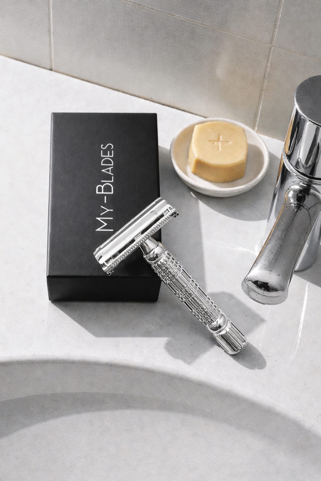 Stainless steel My-Blades double edge safety razor displayed on a bathroom sink next to black My-Blades packaging, shaving soap, and faucet, highlighting a modern men’s grooming routine.